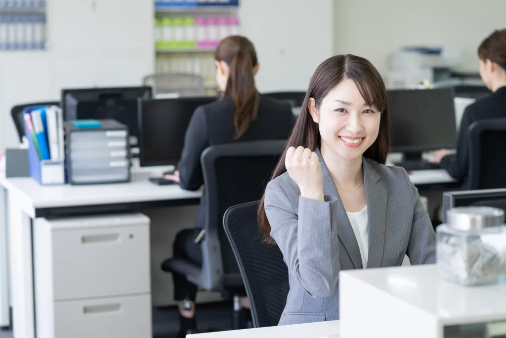 ホームページ制作事務所で、女性スタッフが笑顔でガッツポーズをしている明るい職場風景